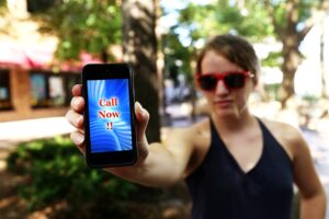 Woman in sunshades holding out a phone with Call Now